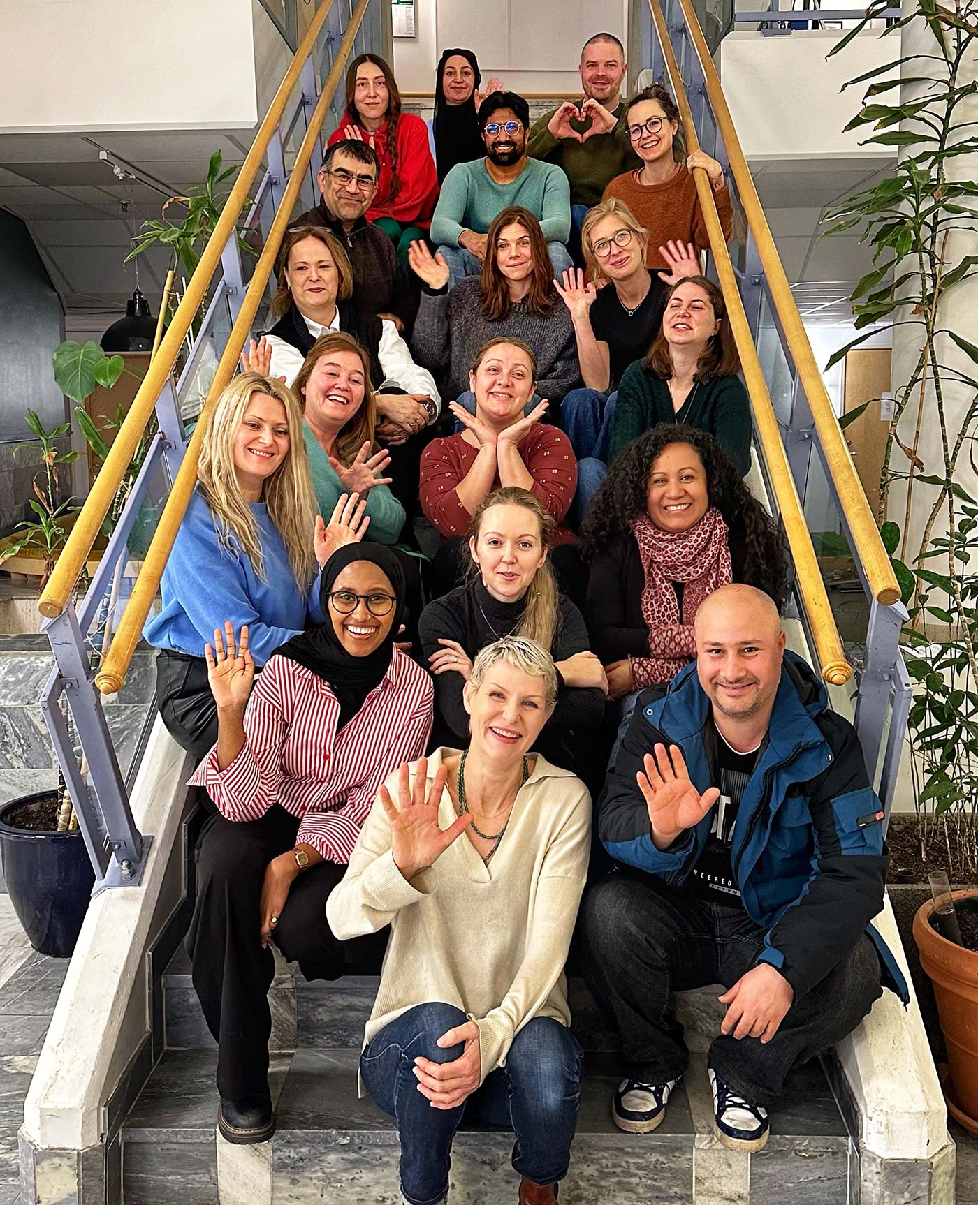 The team at Svenska med baby. Employees sitting on a staircase and waving.